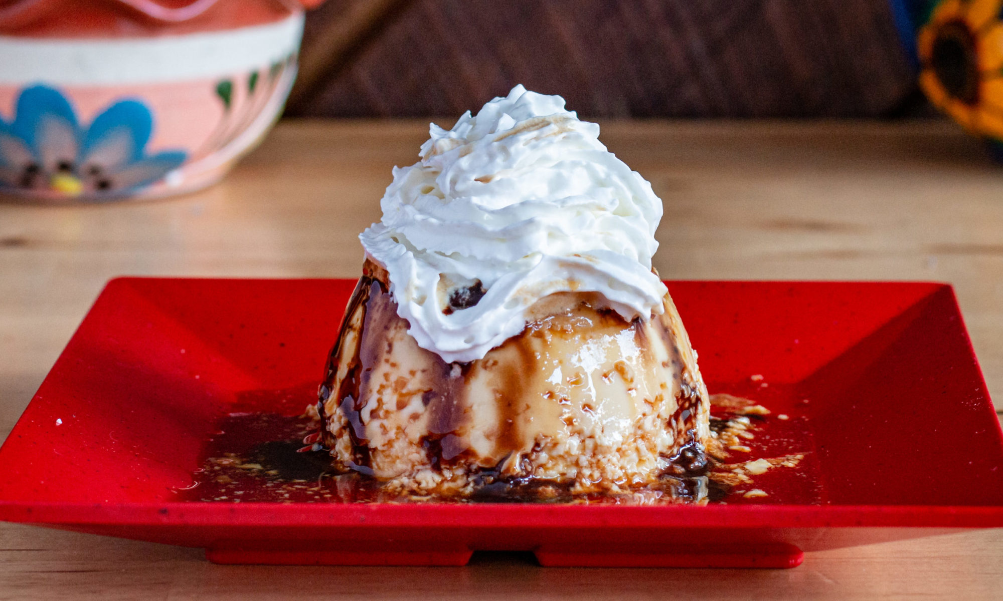 Flan with whipped cream and caramel on a red plate